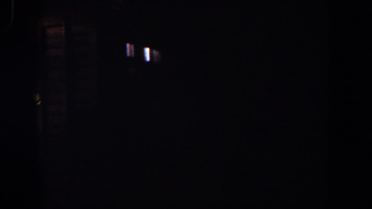 Dark 1958 8mm frame with small light flares, faint vertical streaking, and little identifiable content.