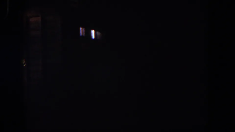 Dark 1958 8mm frame with small light flares, faint vertical streaking, and little identifiable content.
