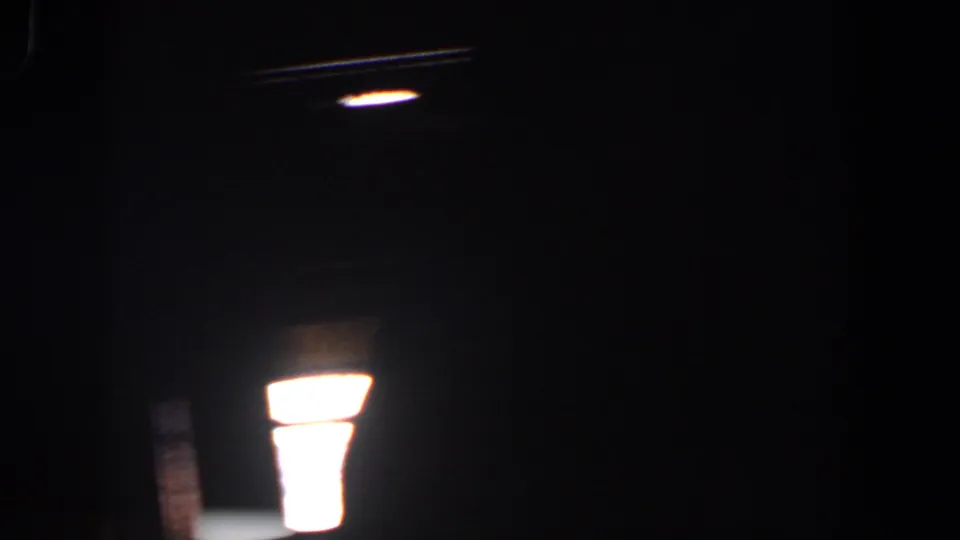 Dark 1958 8mm frame with a bright light flare or projection reflection near the lower center and faint surrounding grain.