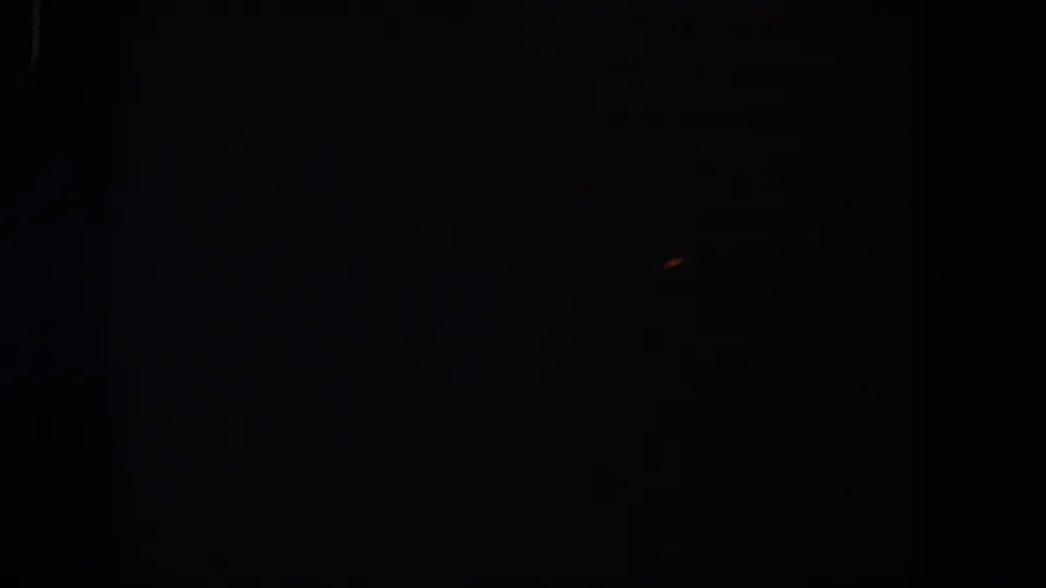 1958 Lubbock 8mm frame showing deep darkness, soft grain, and a small reddish light fleck near the upper right.