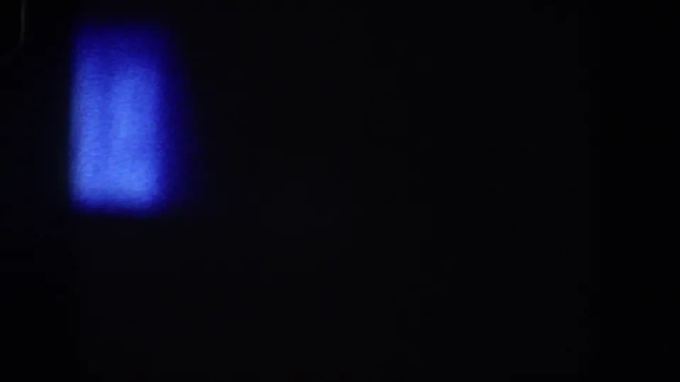 1958 Lubbock 8mm frame with a soft blue glow at lower left, surrounded by darkness, grain, and faint film marks.