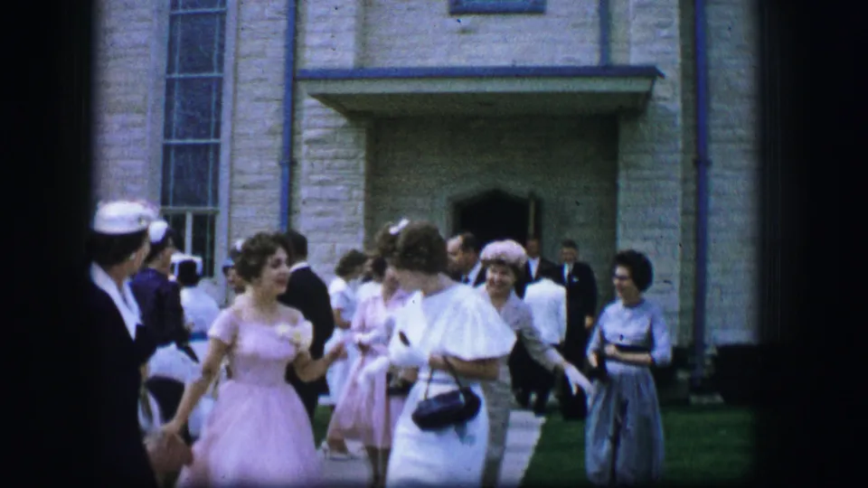 Moberly, Missouri church exterior scene with women in pastel formalwear moving through a small gathering in 1962.