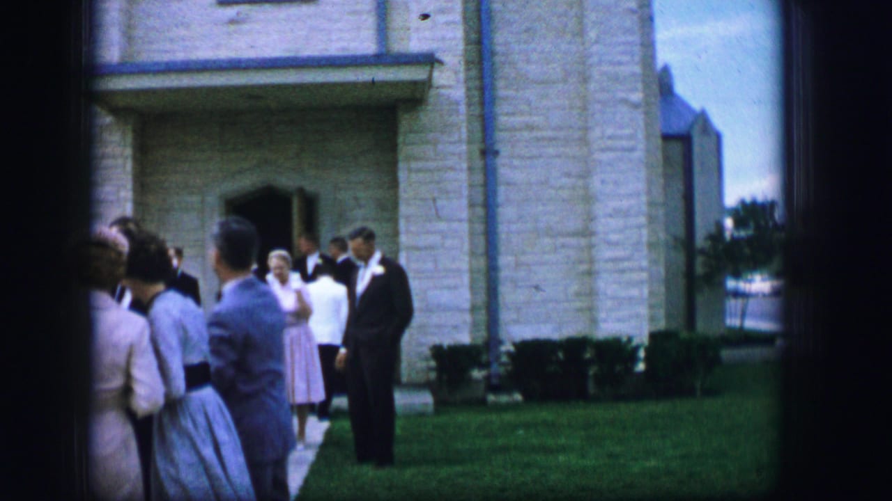 In Moberly, Missouri, 1962, adults in suits and dresses stand near the entrance of a pale stone building on a lawn.