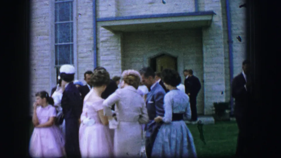 A child in a pink dress stands near adults in formal clothing outside a stone building in Moberly, Missouri, 1962.