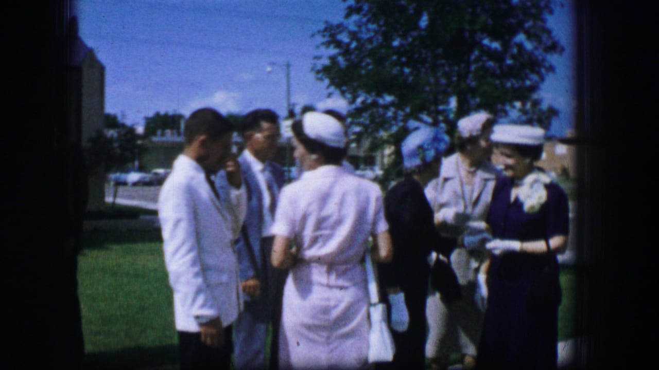 Adults in formal clothing stand talking outdoors in Moberly, Missouri, in 1962, with a woman in a white uniform and cap among them.