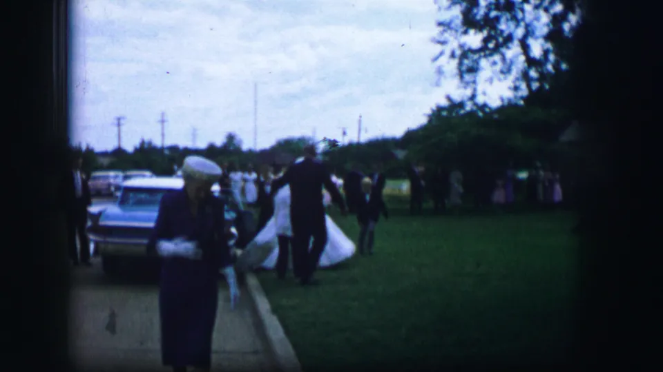 In the final frame, the woman in blue appears to smoke while adults, including a white-dressed figure, move near cars and grass in Moberly.