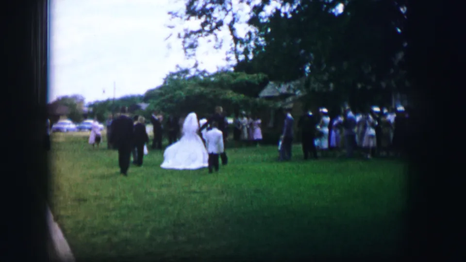 1962 Moberly, Missouri frame showing the bride on a garden lawn with guests assembled near trees and parked cars beyond.