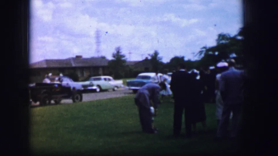 Adults in period clothing gather on a lawn in Moberly, Missouri, with early-1960s cars and trees visible behind them.