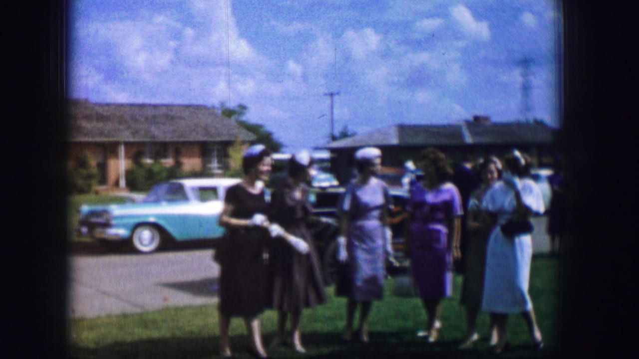 In 1962 Moberly, Missouri, women in mid-century dresses and hats gather outdoors beside parked cars and suburban houses.