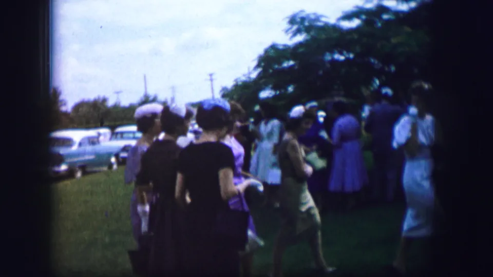 The group continues across the lawn in 1962 Moberly, with women in hats and dresses seen from the side and back near parked cars.