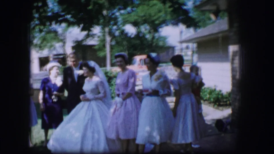 1962 Moberly wedding party outdoors, with the bride, pastel-dressed attendants, and suited guests grouped near a residential street.