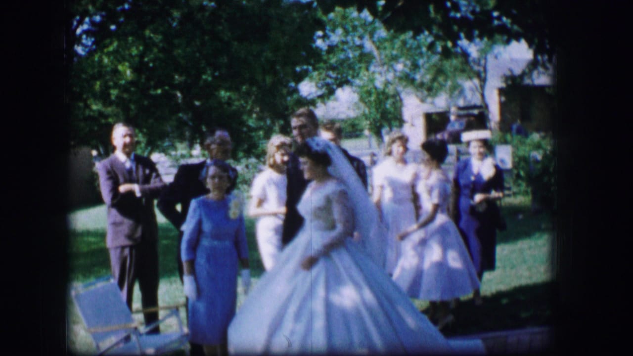 In Moberly, Missouri, 1962, a bride in a white gown and veil walks through a garden as guests watch from the lawn.