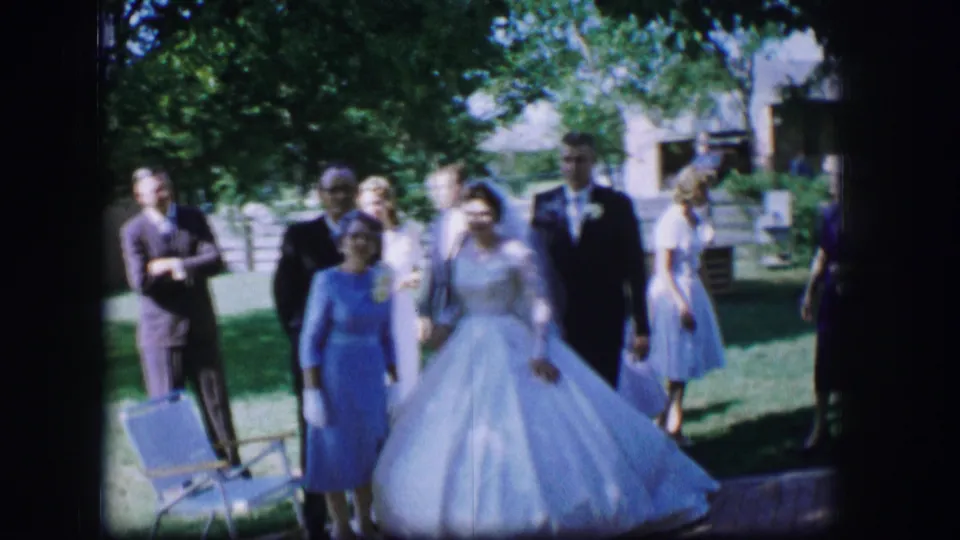 The bride and groom move forward through the Moberly garden wedding scene, followed by guests in pastel dresses and dark suits.