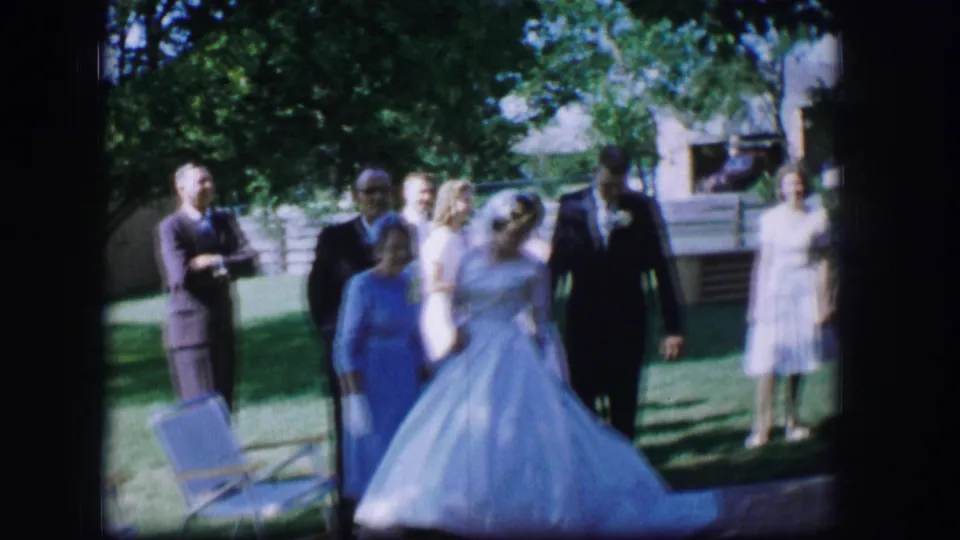 Near the end of the clip, the bride and groom continue across the lawn while guests remain gathered in the garden.