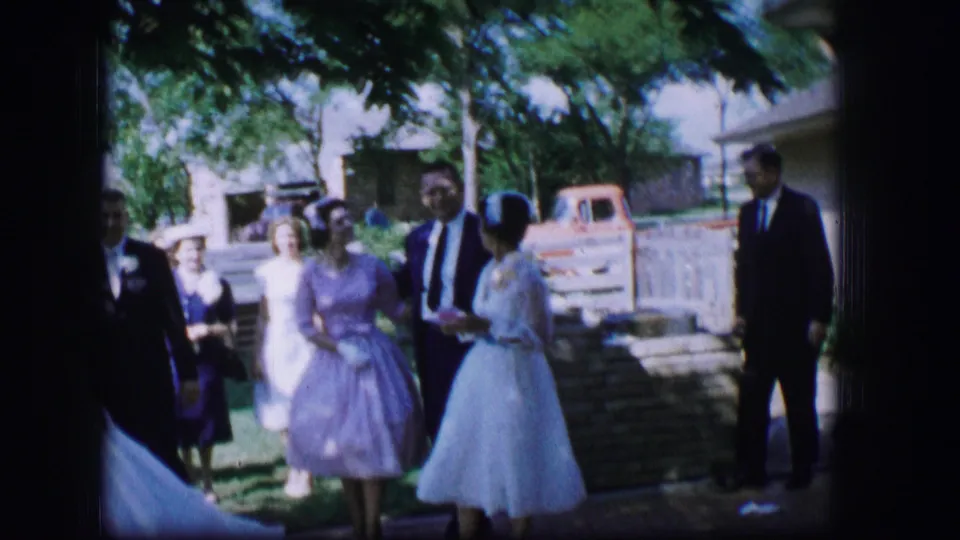 The wedding party gathers on a lawn in 1962 Moberly, Missouri, with the bride, groom, pastel-dressed attendants, and suited guests visible.