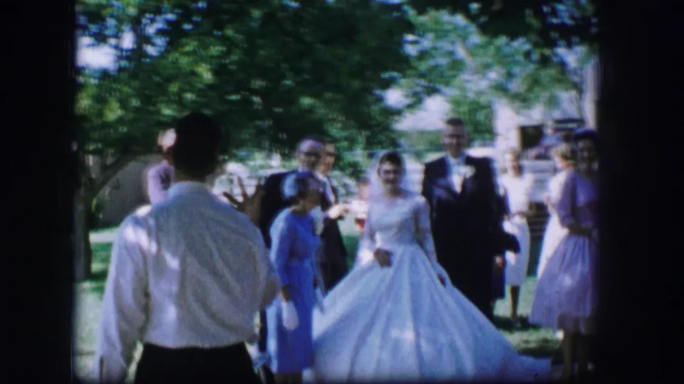 A man in a white shirt is seen from behind as he faces the bride and wedding guests during the 1962 outdoor gathering in Moberly.