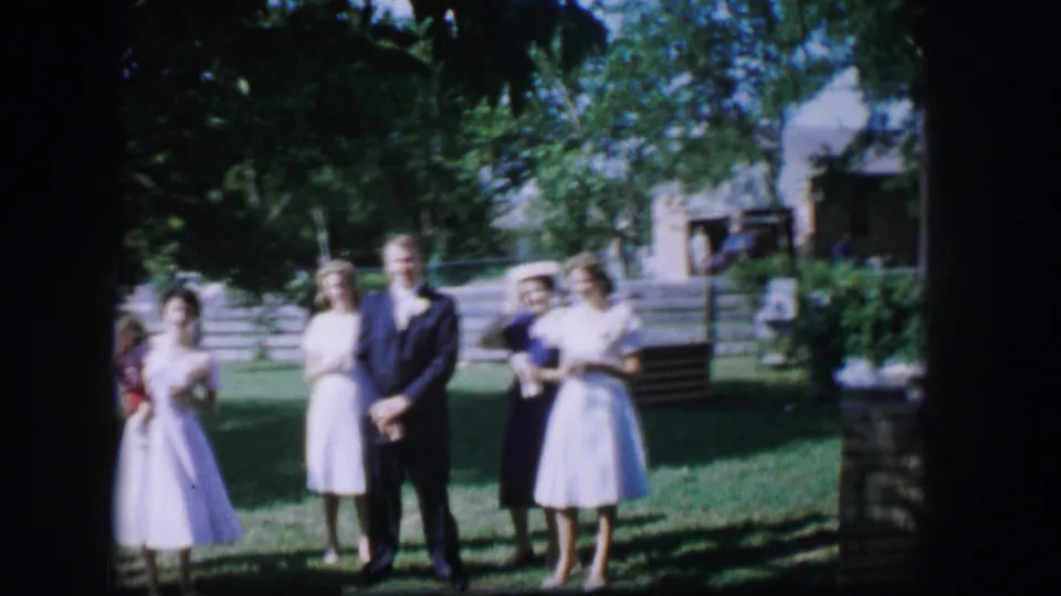 1962 Moberly, Missouri frame with adults in dresses and a dark suit standing outdoors near steps and trees.