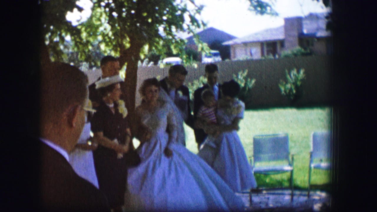 1962 Moberly, Missouri wedding guests gather around a bride in a full gown and a groom in a dark suit on a backyard lawn.