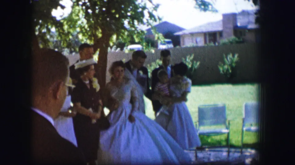 1962 Moberly, Missouri wedding guests gather around a bride in a full gown and a groom in a dark suit on a backyard lawn.