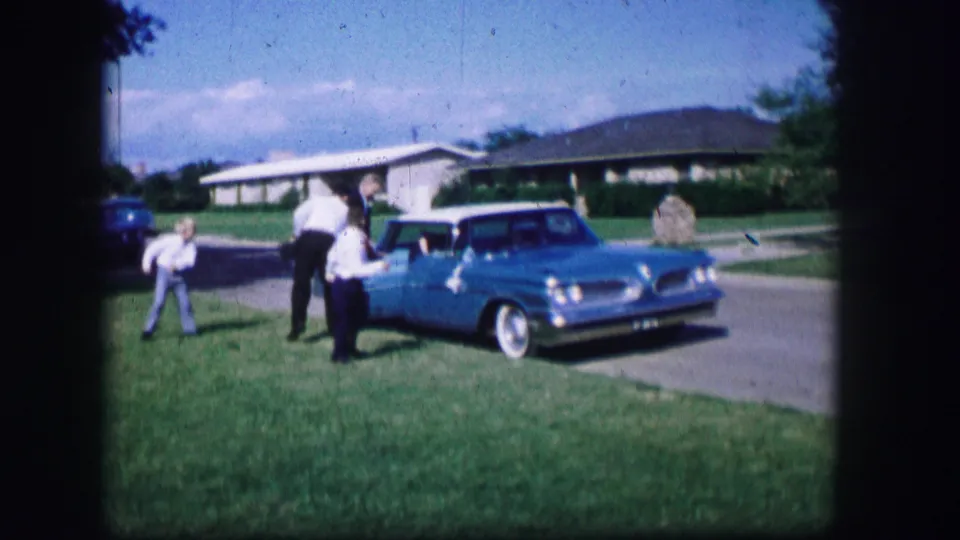The home movie follows guests near a blue station wagon on a residential street during the 1962 Moberly wedding gathering.