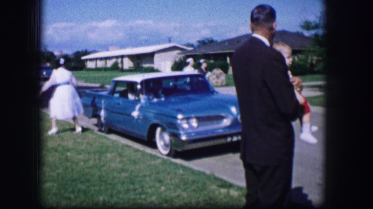 In 1962 Moberly, Missouri footage, a blue Pontiac sits at the curb while several people gather on a sunny residential street.