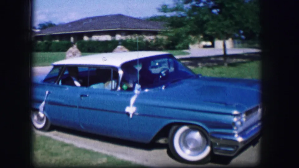 The car passes in side view on a residential street, showing the blue body, white roof, chrome details, and whitewall tires.