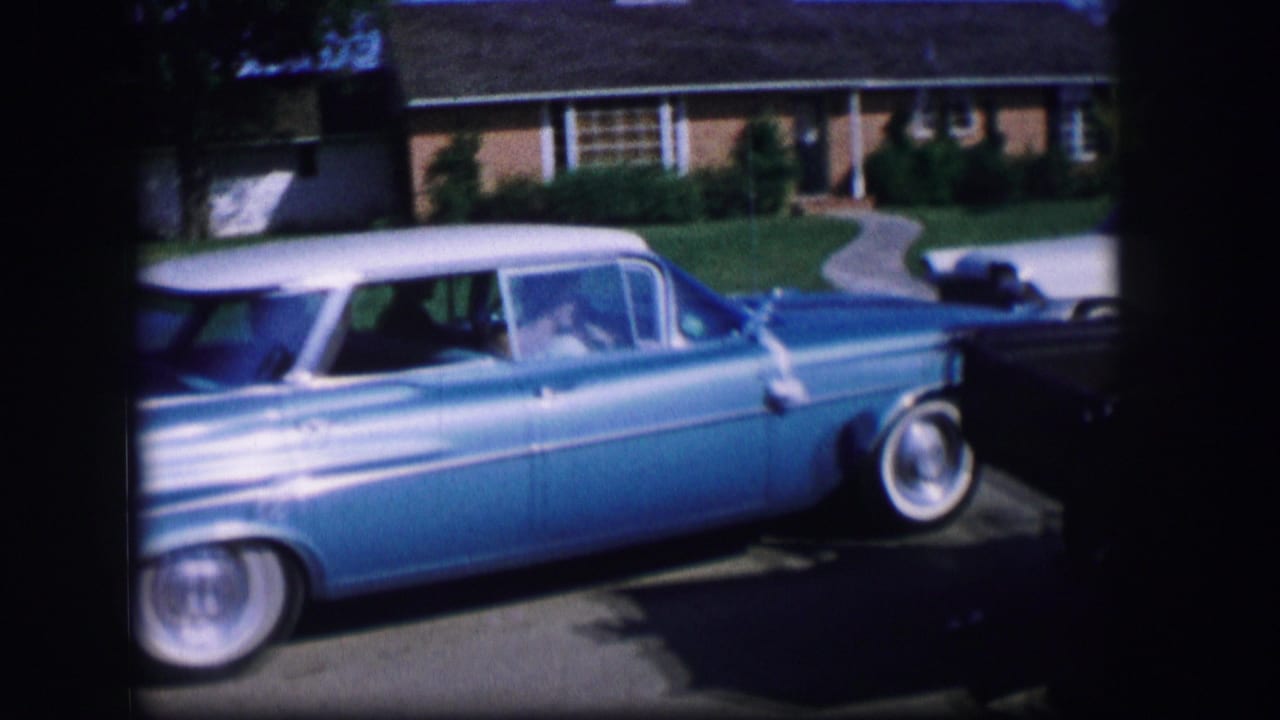 Blue classic car seen from the side near a driveway and house.