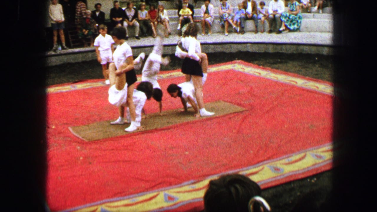 Performers form a human-pyramid base on a red carpet while spectators sit behind them.