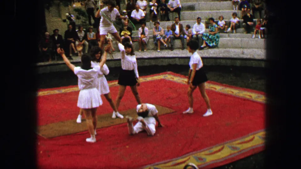 Final frame shows an elevated acrobatic pose above the red carpeted stage, with other performers and seated spectators in the background.