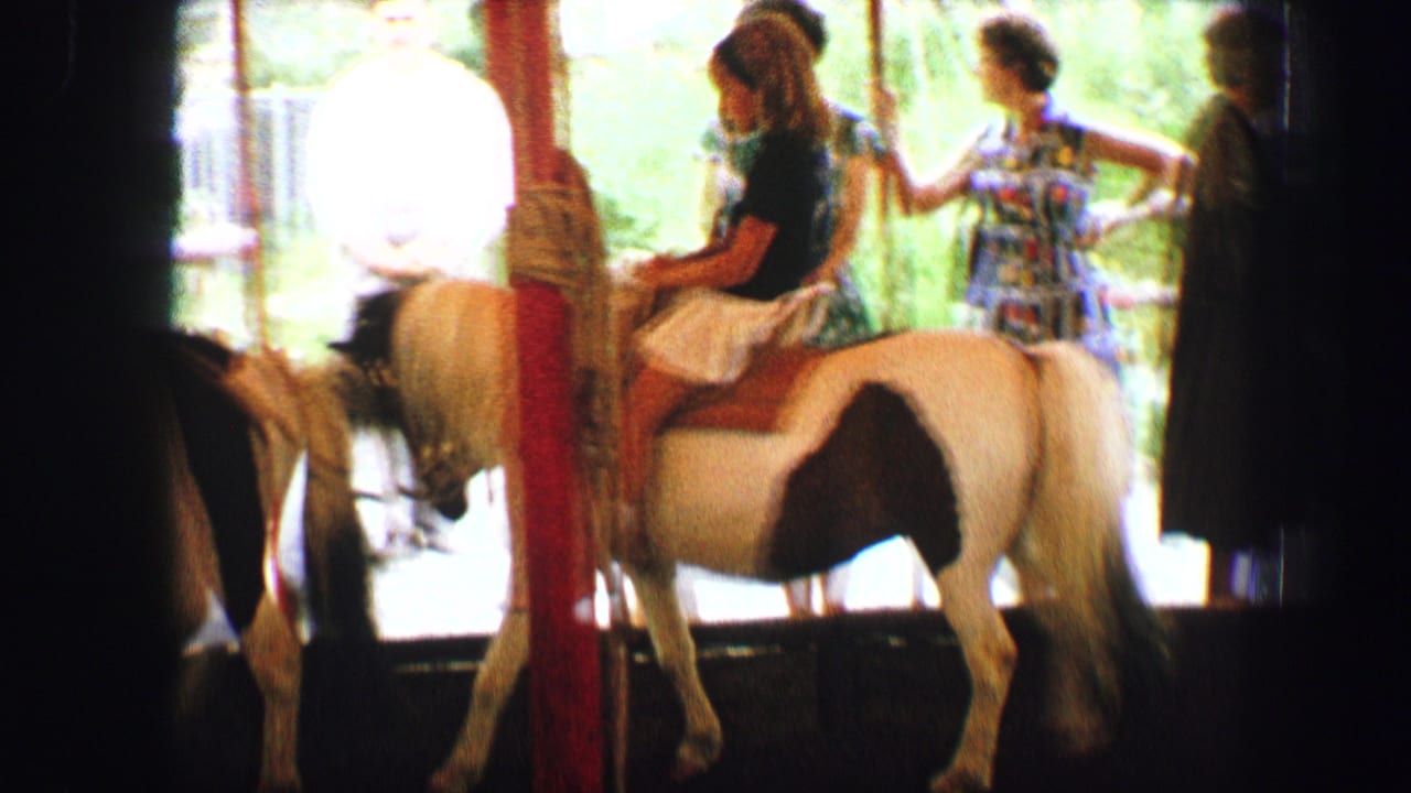 1963 Austria home-movie frame showing children near white ponies on a shaded outdoor pony ride with adults nearby.