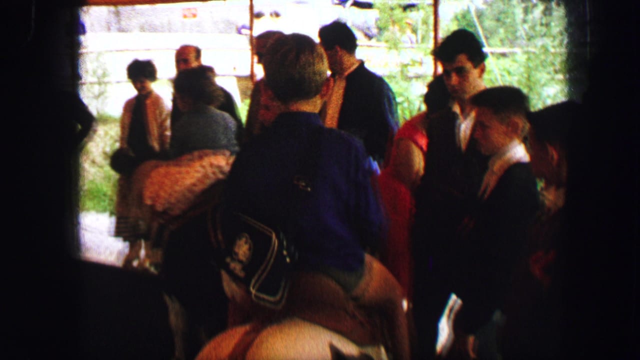 1963 Austria home-movie frame showing people gathered around children on small horses under a shaded pony-ride structure.