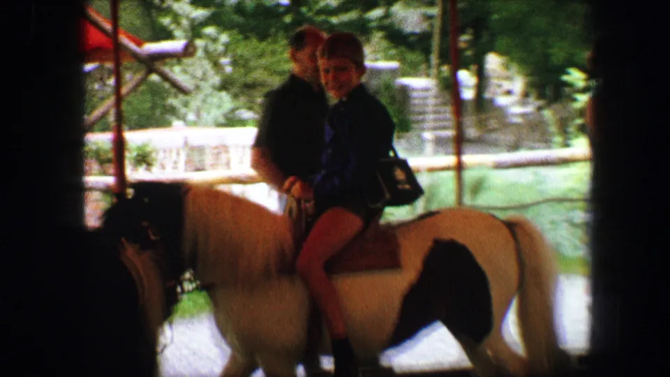 Two children sit on a small horse near greenery and a water feature in the 1963 Austria pony-ride footage.