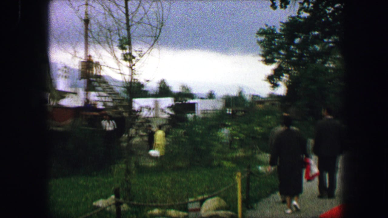In Austria, 1963, adults and a small child move through a green public garden with wooden play structures in the background.