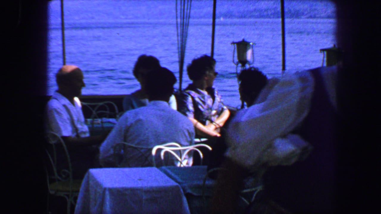 Restaurant patrons sit near large windows as a waiter passes in shadow.