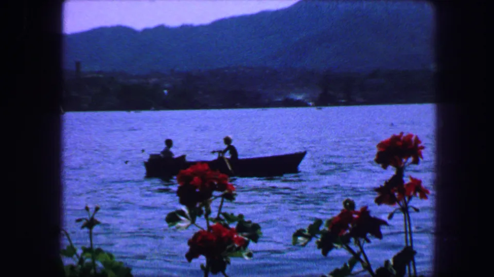 1963 Lucerne waterfront view from the restaurant, with red flowers in the foreground and a rowboat on the water.