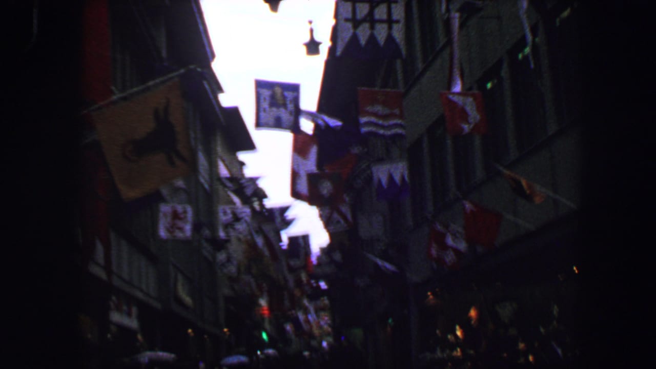 Dark narrow street lined with flags and pedestrians in the distance.
