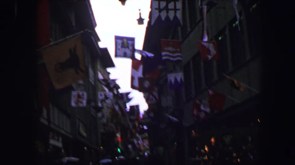 Lucerne city street in 1963, seen through dim 8mm exposure with hanging flags, building facades, and pedestrians farther down the road.