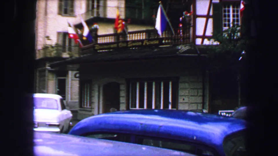 1963 Lucerne street frontage showing flags above a building entrance, parked mid-century cars, and older hotel architecture.