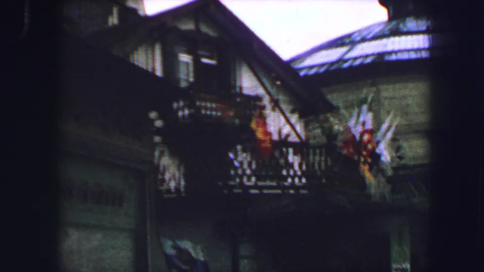 Lucerne building facade with dark timber balconies, colorful flags, and adjacent rooftops in 1963 travel footage.