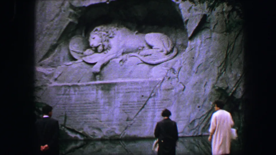 Lucerne Lion Monument scene with adult visitors seen from behind before the carved lion relief in the rock face.