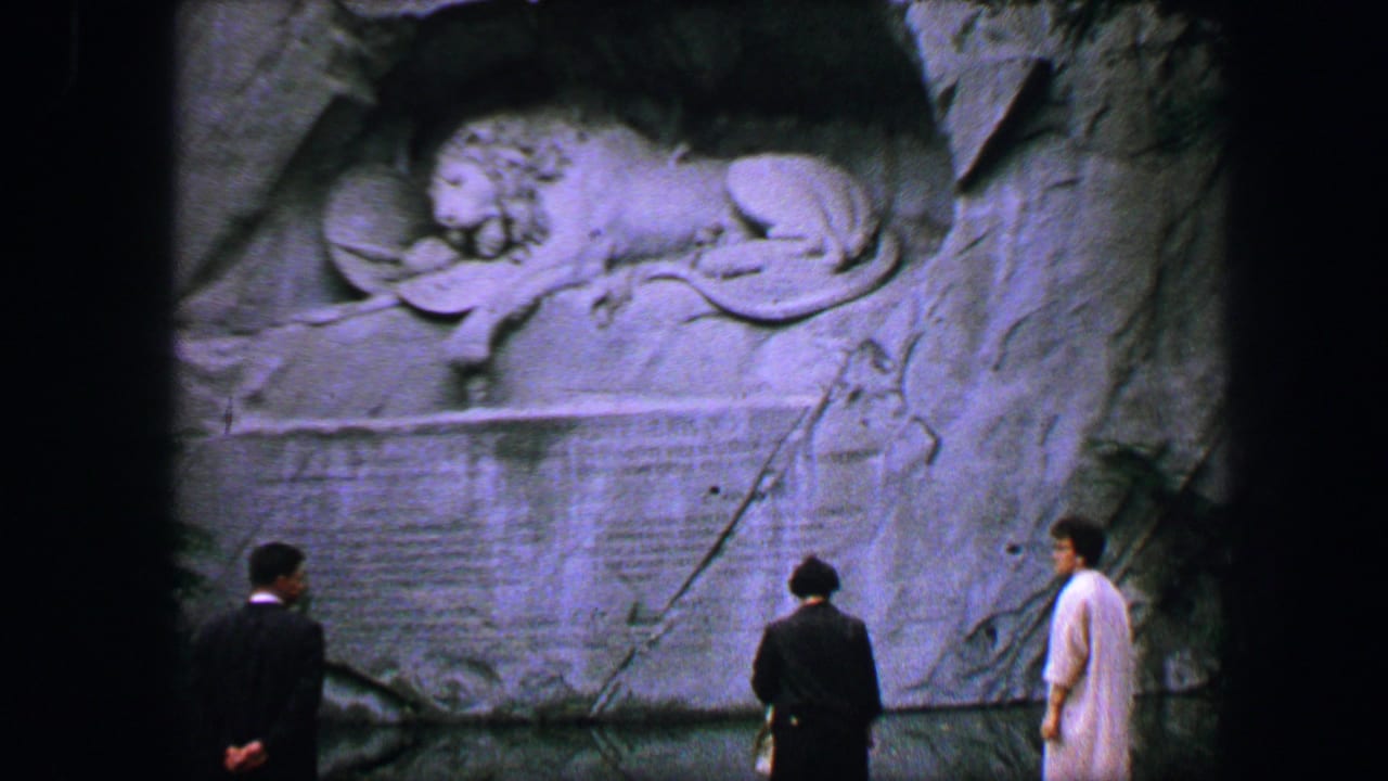 1963 Lucerne home-movie frame showing three visitors viewing the carved Lion Monument memorial in the rock wall.