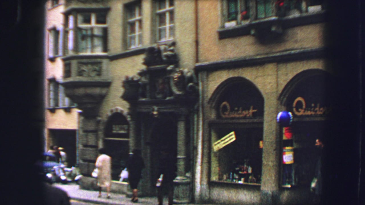 Street view of ornate building facade with pedestrians and a parked car.