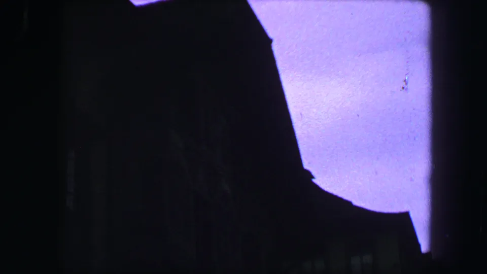 Dark 8mm frame from Lucerne with roofline silhouette, faint windows, and pale sky dominating the upper view.