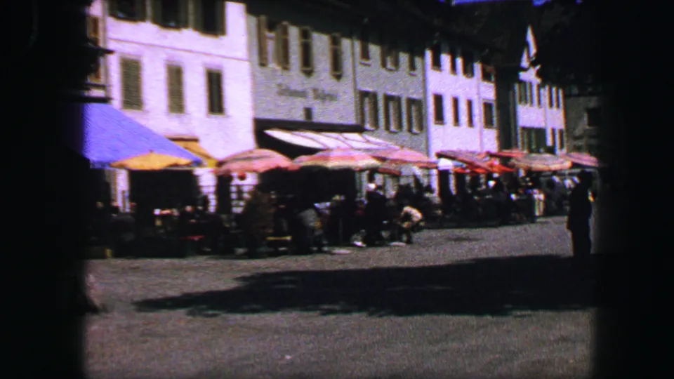 1963 Lucerne street cafe area with umbrellas, pedestrians, awnings, and multi-story town buildings.