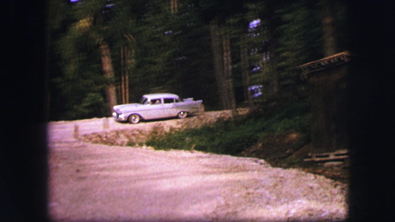 Grey mid-century car on a quiet wooded road near Saint Moritz, Switzerland, in 1963 home-movie footage.