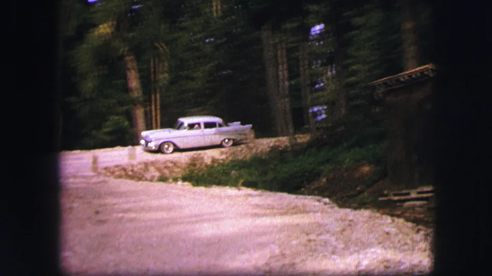 Grey mid-century car on a quiet wooded road near Saint Moritz, Switzerland, in 1963 home-movie footage.