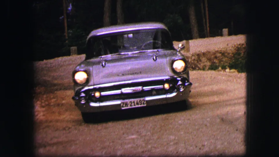 1963 Saint Moritz home-movie frame showing a silver Chevrolet Bel Air approaching the camera on a roadside curve.