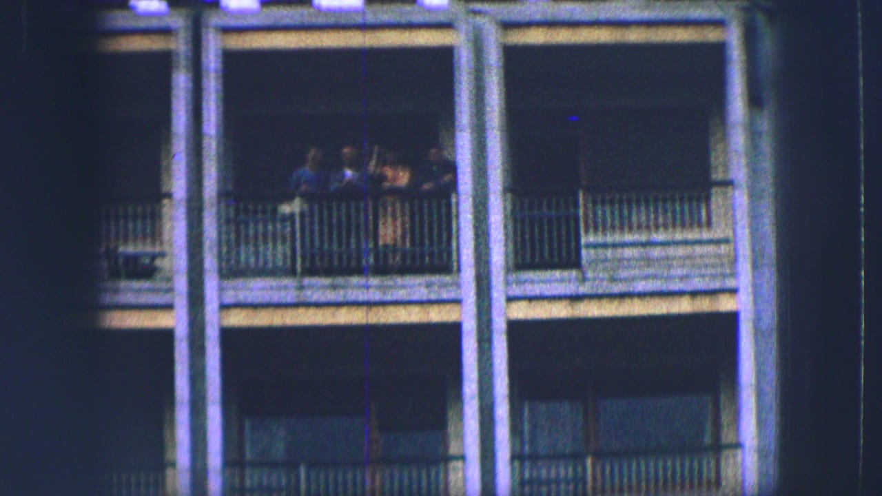 Four people stand on a balcony of a yellow-gray building in Saint Moritz, seen in soft 1963 8mm footage.
