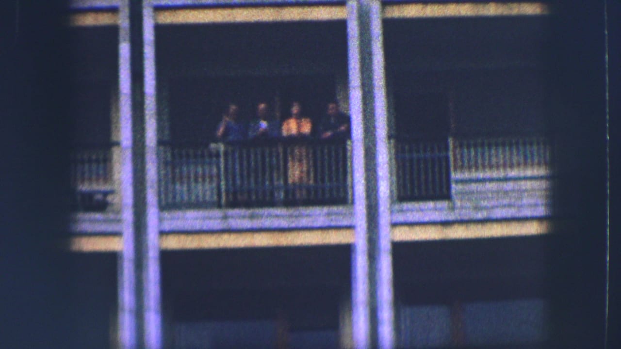 People grouped at a balcony railing between tall exterior columns.