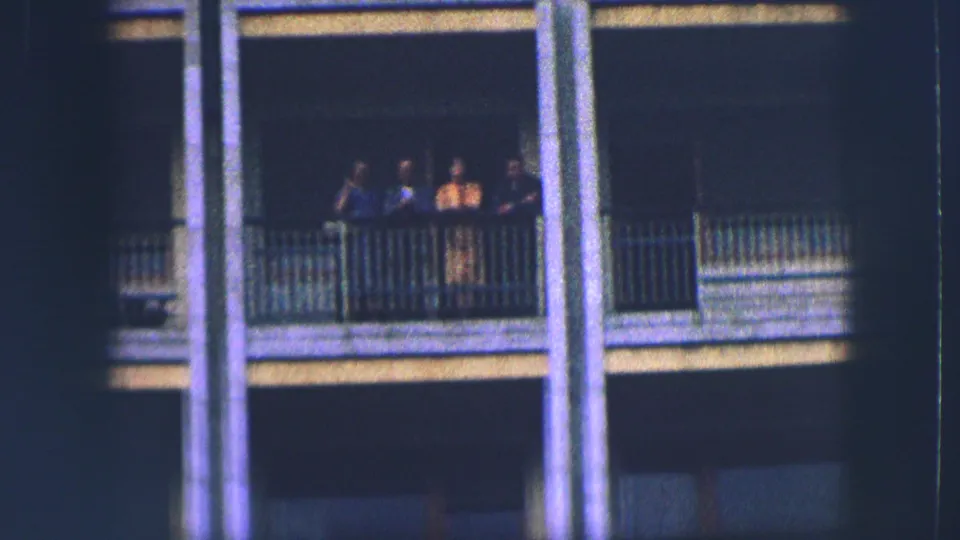 A distant balcony group stands between vertical columns on a Saint Moritz building exterior in 1963 home-movie footage.